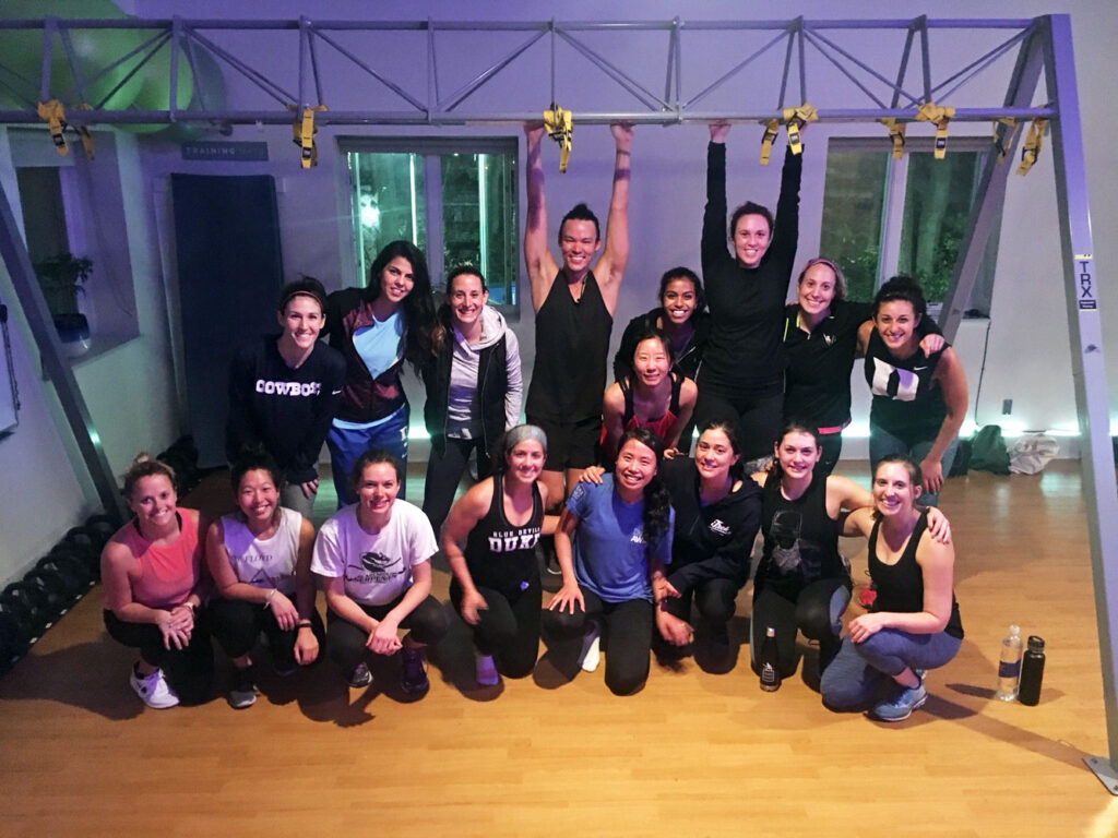More than a dozen students, mostly comprised of some of the women at Fuqua, pose after a workout at a Durham gym