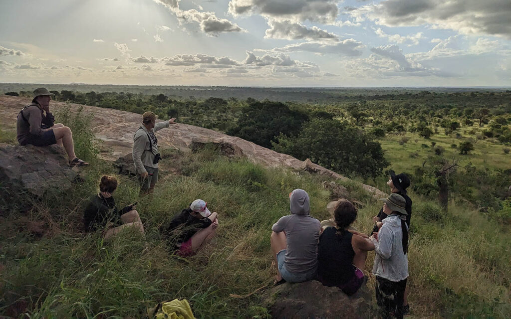 A group of Duke students sit on a grassy hillside in Kruger National Park in South Africa