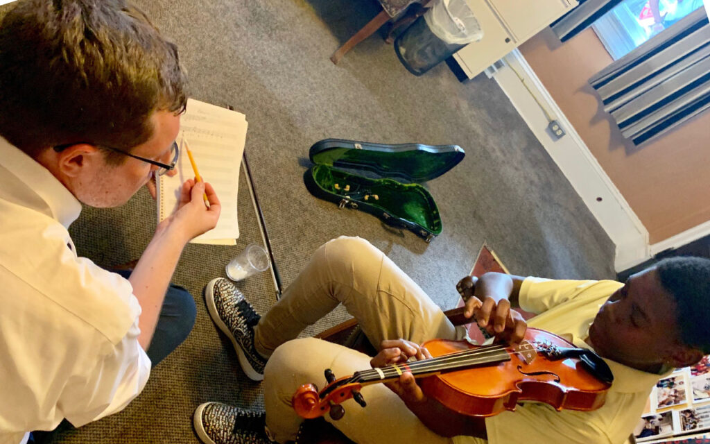 Ryan Van Slyke points at written music, next to a young boy playing the violin