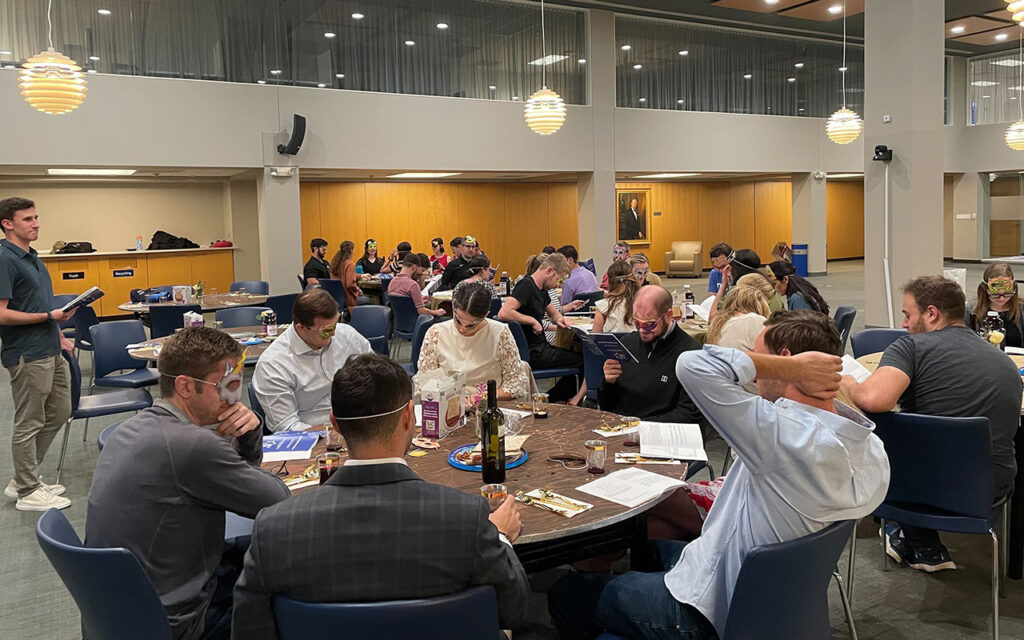 Dozens of people sitting at large round tables for Passover Seder in Kirby Reading Room at Duke University's Fuqua School of Business