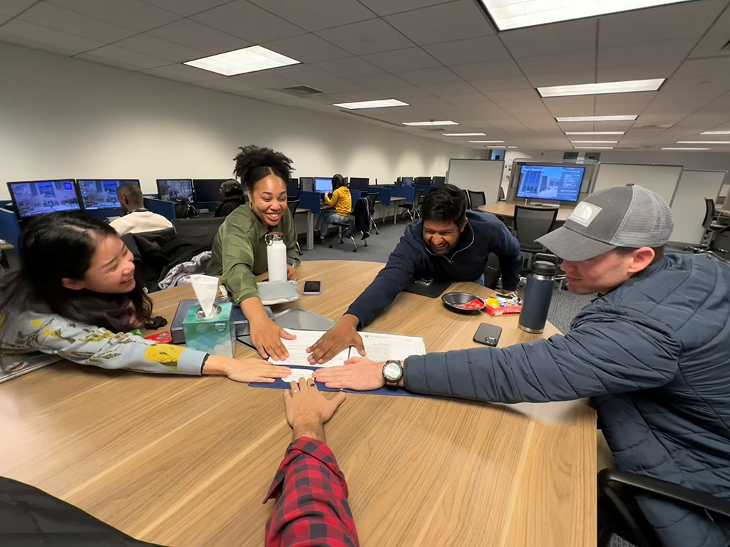 Gerard Pozzi and his teammates in the Daytime MBA Class of 2025 put their hands into the middle of a table at Duke University's Fuqua School of Business