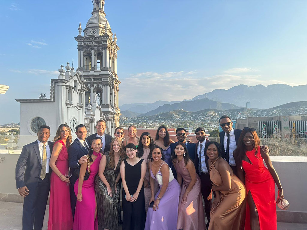 A group of students dressed in wedding attire, a historic building and mountain range in the background