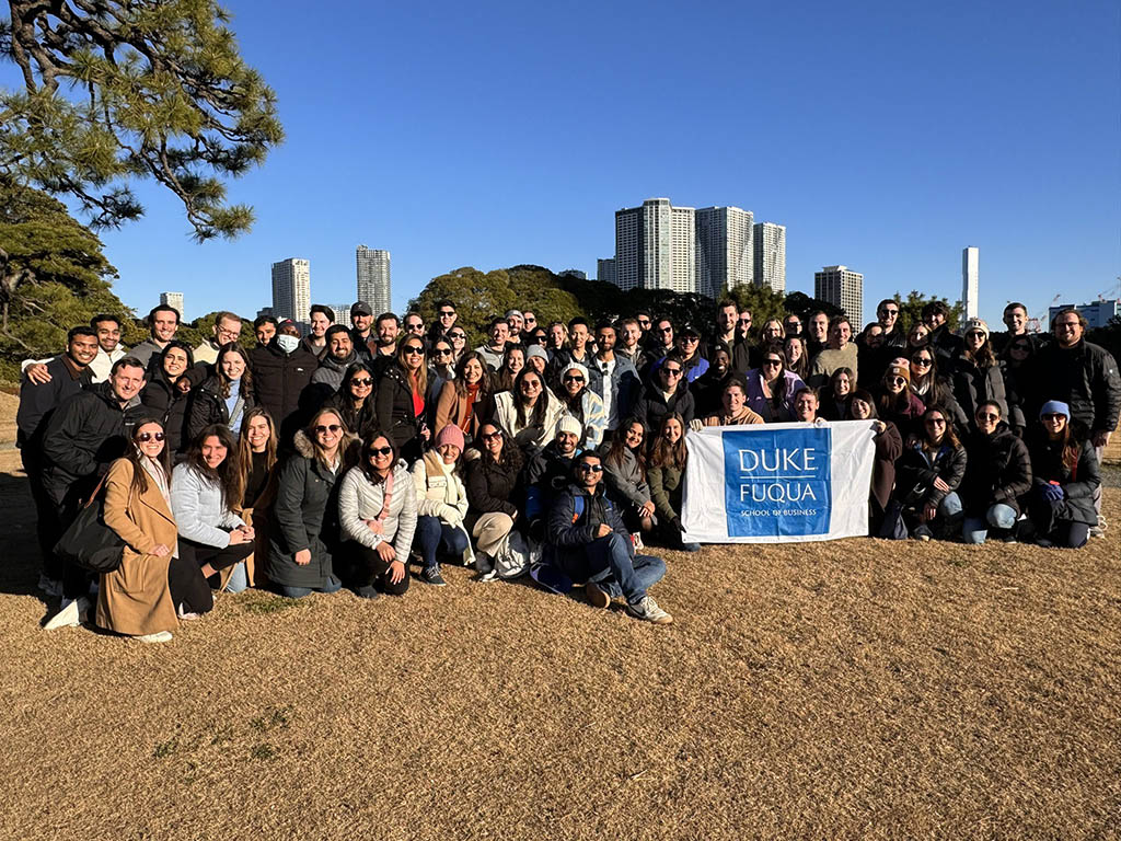Group photo of dozens of students in Japan, someone in the center of the group is holding a white and blue Fuqua flag