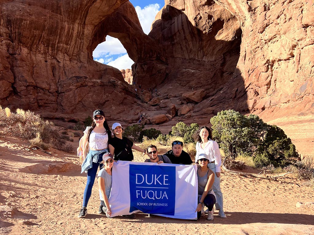 Amanda Shamirian and her MBA classmates holding a white flag with a blue Duke Fuqua logo on a hiking trail in Utah