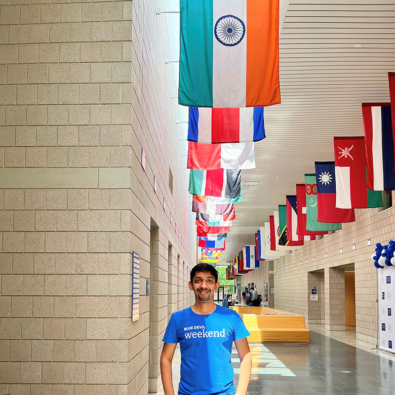 Kunj Chheda, a student in the Daytime MBA program, standing underneath the Hall of Flags at Duke University's Fuqua School of Business