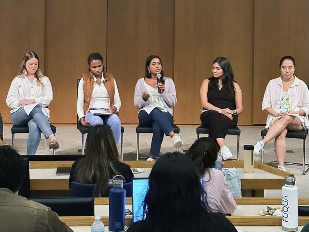 Monika Palabindela and four of her classmates sitting at the front of an auditorium for a panel at Duke University's Fuqua School of Business