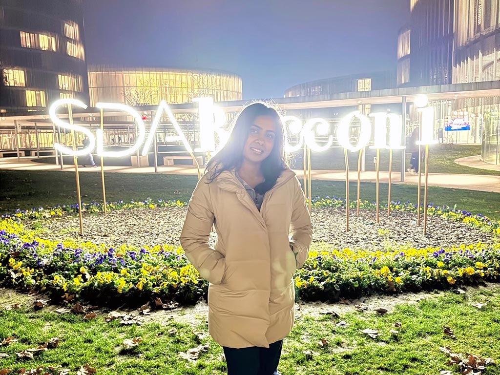 Monika Palabindela stands in front of a light display reading "SDA Bocconi" at night time