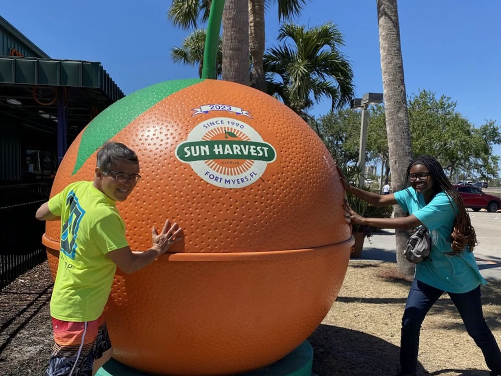Jasmine Alexander, a student at Duke University's Fuqua School of Business, and her professor each stand on opposite sides of a giant orange sculpture in Fort Myers, Florida
