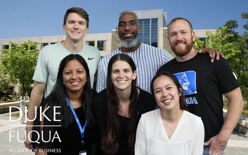 Six students, three men and three women, stand in front of virtual background showing Duke University's Fuqua School of Business