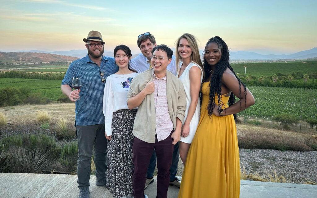 Six Global Executive MBA students pose for a photo in Santiago, Chile. Mountains and a winery are in the background.