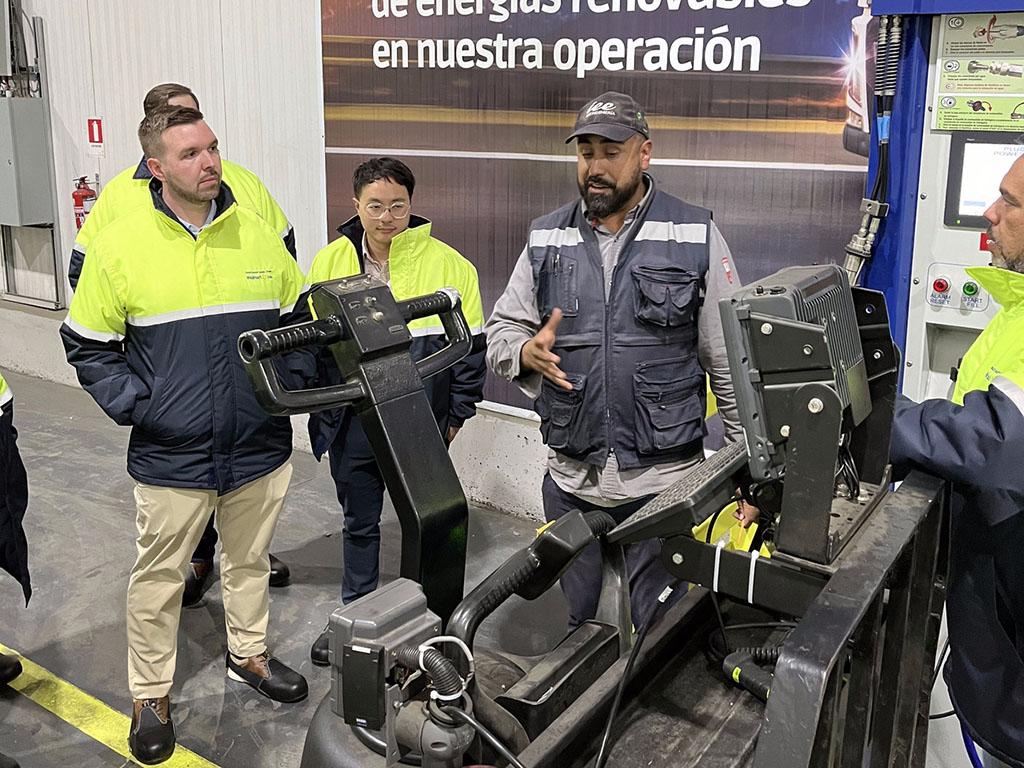 Matt Engle and a few of his classmates wear reflective jackets and stand around a piece of equipment at the Walmart hydrogen plant in Chile