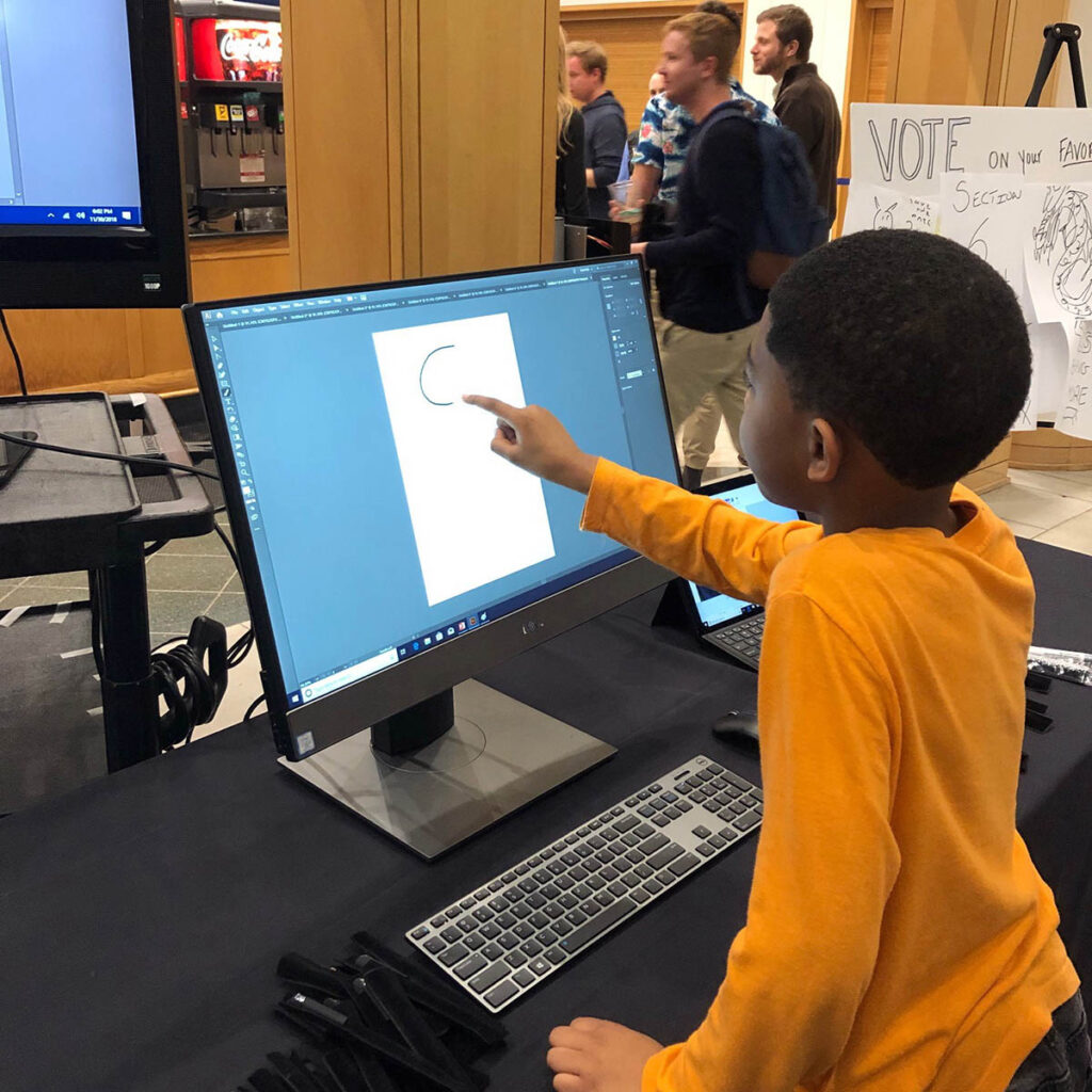 A young boy using his finger on the computer screen to draw