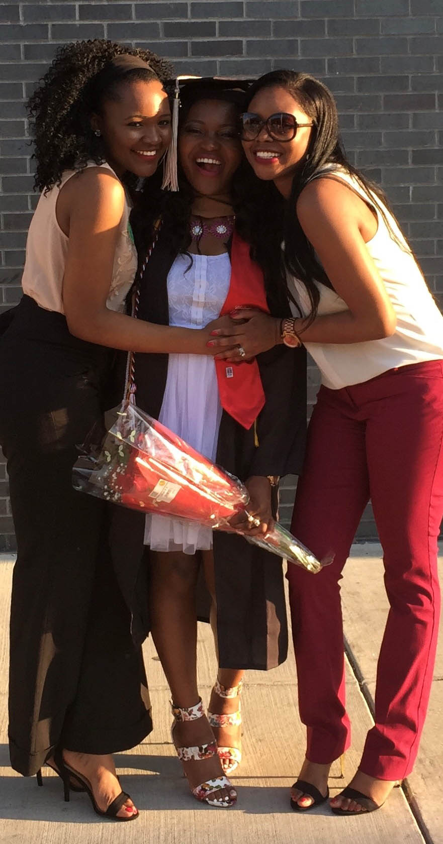 Three ladies posing arm in arm, with the lady in the middle dressed in a graduation cap and gown; How My Background Prepared Me to Attend Fuqua