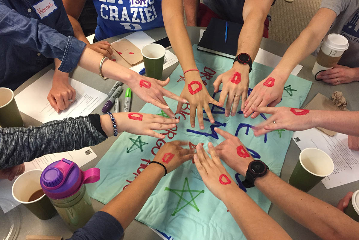 A number of hands touching, with the letter "D" painted on them; diversity and inclusion