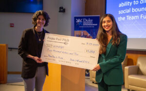 Daytime MBA student Arya Diwase wins Fuqua Fast Pitch competition, she stands on stage at Duke University's Fuqua School of Business holding her winnings alongside Professor Jamie Jones