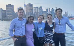 Stephanie Blair with four of her MBA classmates at Duke University's Fuqua School of Business. They are standing against a railing with water and the New York skyline behind them.