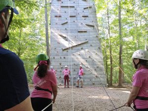 A handful of Fuqua students stand near a high climbing wall at an outdoor obstacle course