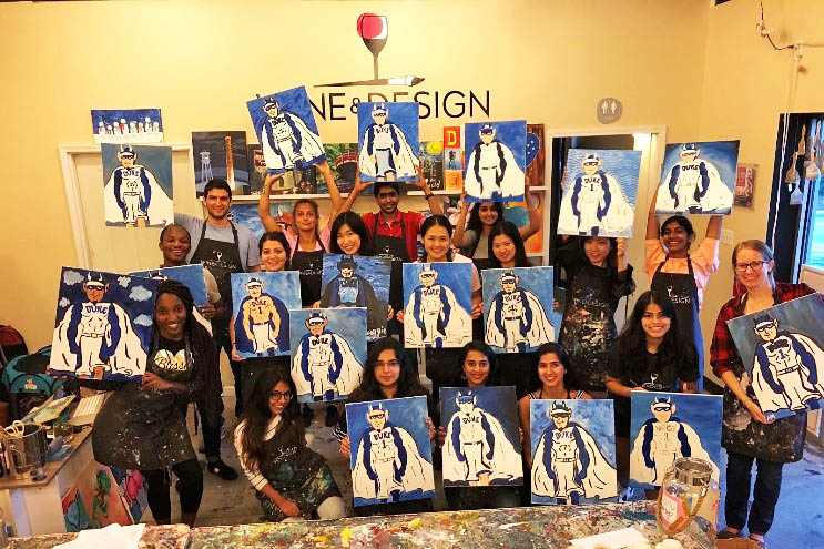 a couple dozen students holding up the Duke Blue Devil paintings they did during one of their student events
