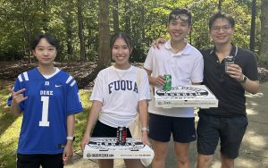 Rachel Peng wearing a Duke football jersey, standing to the left of three friends, also wearing Duke athletics attire. Two are holding pizza boxes.
