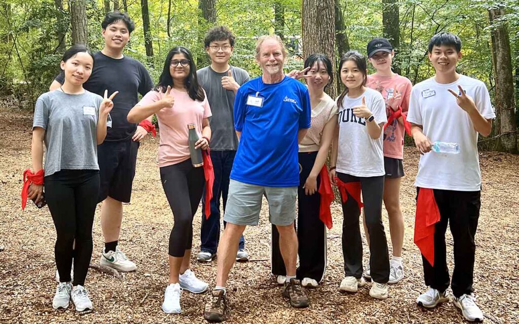Kylie Lin with a handful of classmates stand in a group in a cleared field surrounded by trees