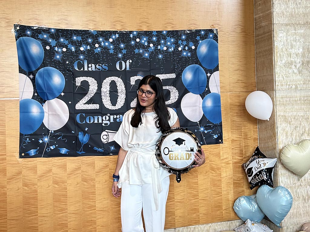 Ashima Garg, an MMS: DKU student at Duke University's Fuqua School of Business, standing in front of a banner reading "Class of 2025 - congratulations!"