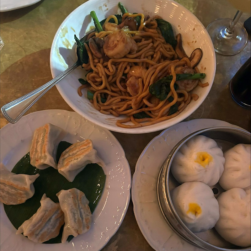 A wooden table displays a few dishes, including steamed and fried dumpings and noodles