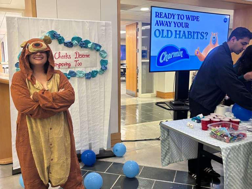Sherya, a Fuqua student wearing a bear costume in front of a display booth set up at the Fuqua Brand Challenge competition at Duke University's Fuqua School of Business