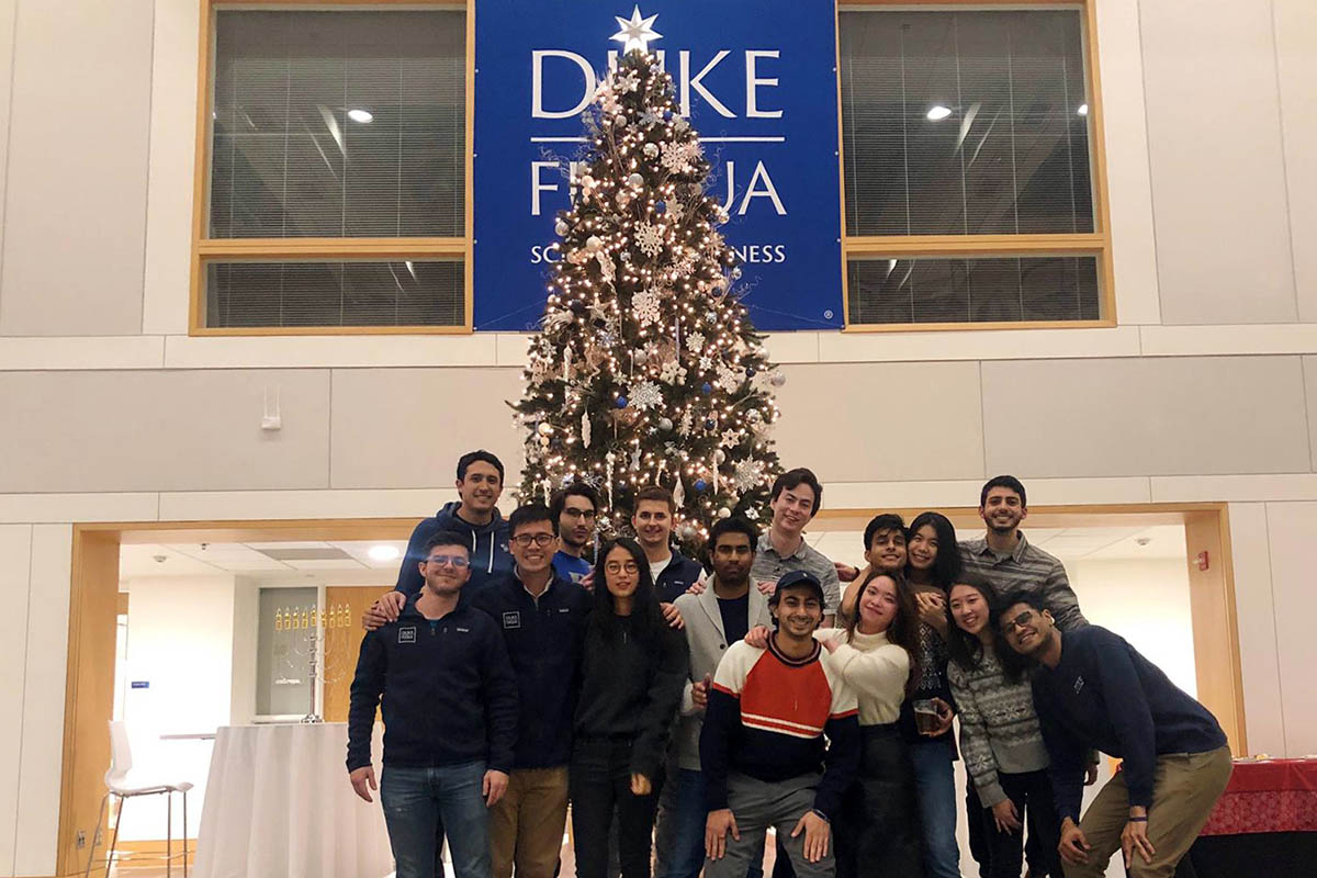 a dozen students standing in front of the Christmas tree and the Fuqua sign in the Fox Center during Fuqua Friday