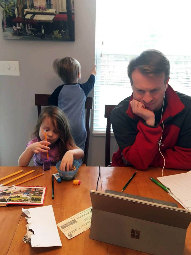 Jamie with headphones on focused on his computer while his two small kids play in the background