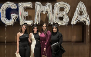 Four Executive MBA students in front of balloons spelling EMBA