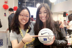 Bella, holding a signed Coach K basketball, with her classmate at a program event, but still not her favorite MQM experience