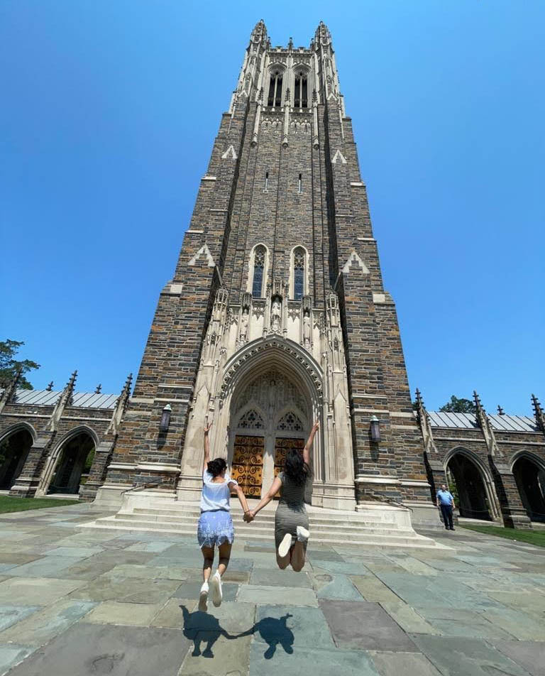 Ritu and a classmates jumping with hands held in front of Duke Chapel