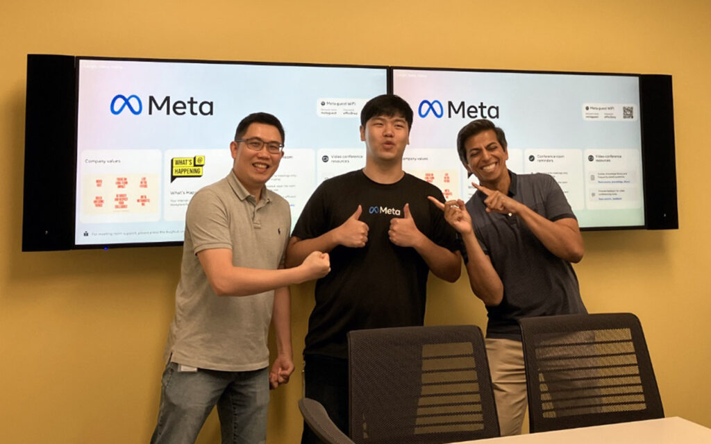 Changhyeon Yoo, an alumnus of the MQM: BA program, standing between two teammates in front of a monitor reading "Meta"