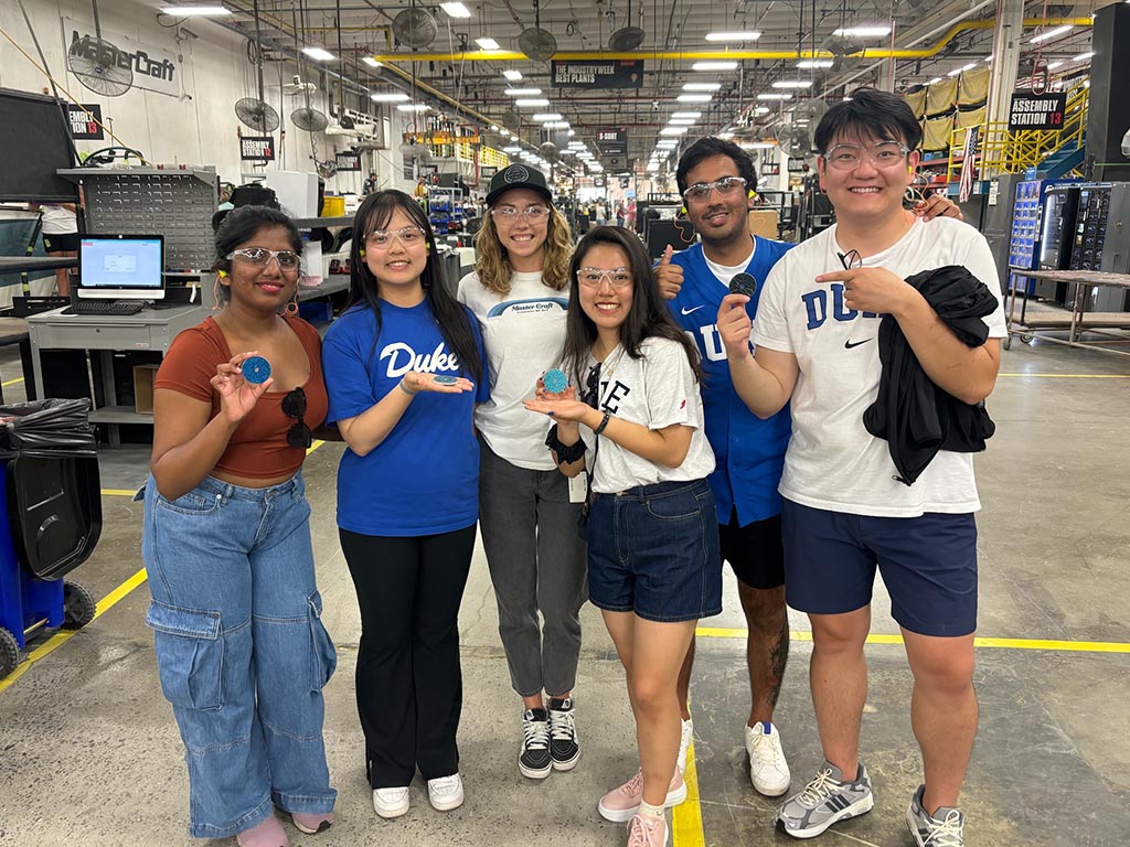 Betty Sum and four of her MQM capstone teammates with alumna Shelby on the floor of the MasterCraft facility