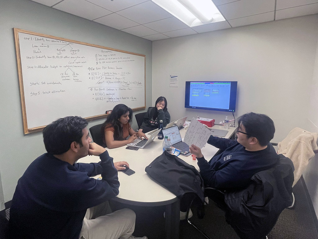 Betty Sun and four of her MQM capstone teammates gather around a conference room in one of Fuqua's team working rooms