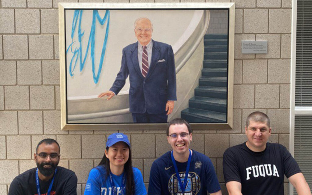 Huyen Nguyen and three of her classmates in the MSQM: BA program at Duke University's Fuqua School of Business kneel under a portrait of longtime Fuqua dean Doug Breeden