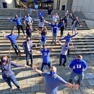 a few dozen of Gavin's MBA classmates standing on the Fuqua entrance stairs, wearing masks and physically distant